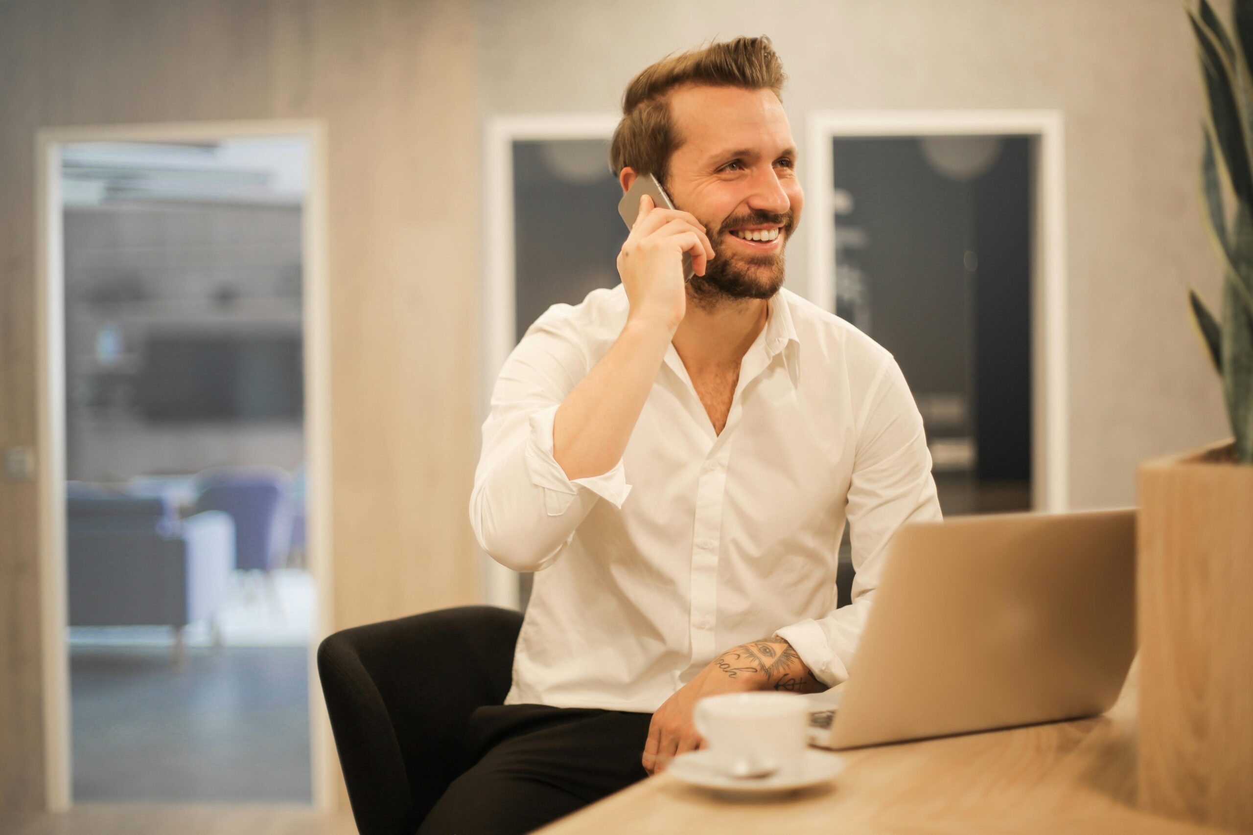 happy-businessman-in-white-shirt-on-phone-call-at-modern-office-desk-with-laptop