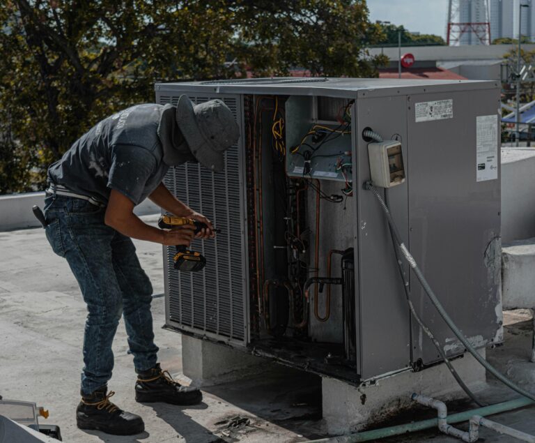 a-worker-in-a-bucket-hat-repairs-an-outdoor-air-conditioning-unit-on-a-rooftop