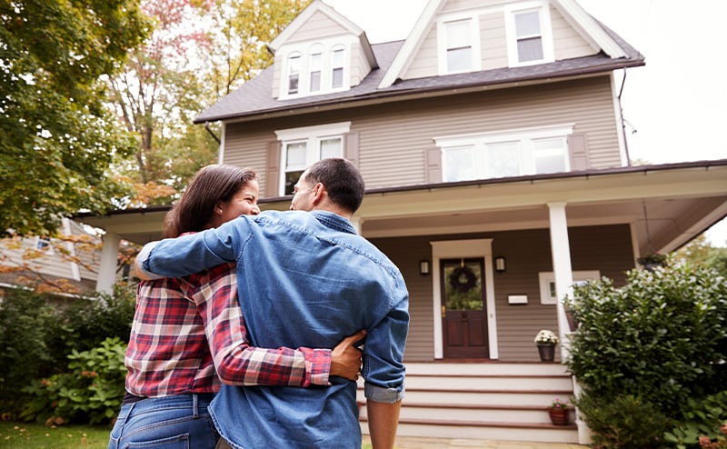 a happy couple outside looking at their new home they bought