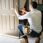 handyman fixing a door with a toolbelt on him and a drill in hand