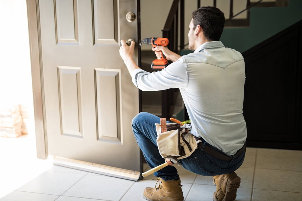 handyman fixing a door with a toolbelt on him and a drill in hand